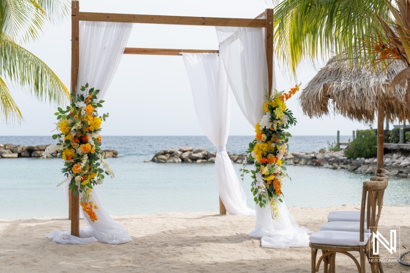 A Beautiful Beach Wedding Setup With Floral Decorations and Flowing Fabric Near Calm Waters Under a Clear Sky at a Tropical Location