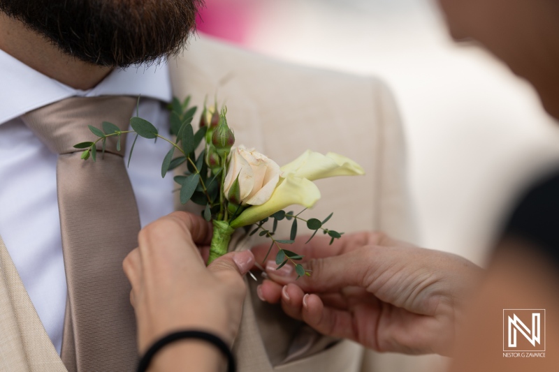 A Wedding Attendant Pins a Delicate Boutonnière Onto the Lapel of a Groom’s Suit in an Outdoor Setting, Capturing the Moment\'s Elegance During the Ceremony Preparations