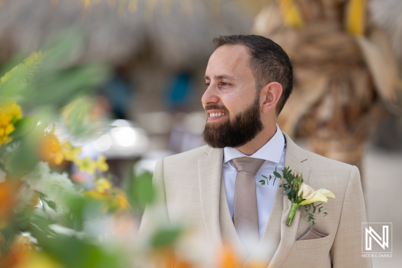 A Groom Stands Smiling Among Vibrant Flowers at a Tropical Outdoor Wedding Venue, Radiating Joy on His Special Day