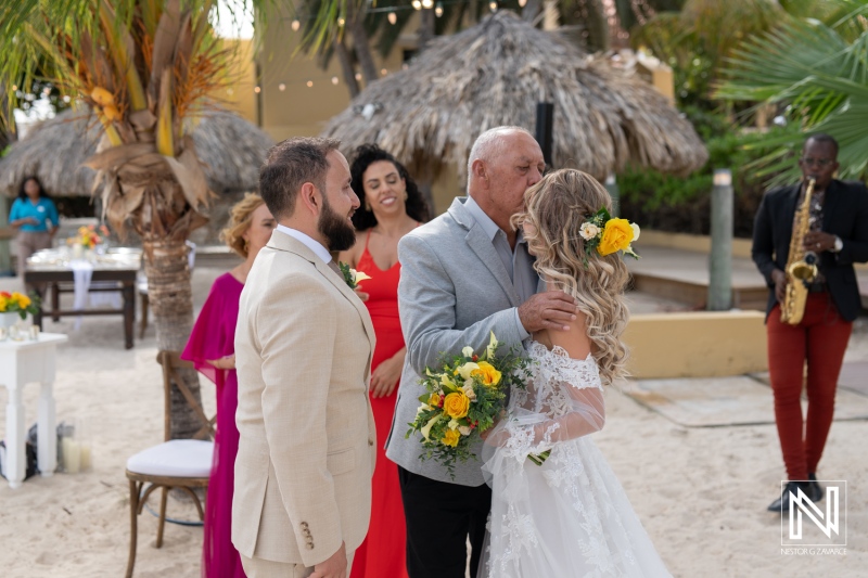 A Beautiful Beach Wedding Ceremony Takes Place at a Tropical Location, Featuring a Loving Embrace Between the Bride and Her Father While Guests Celebrate in the Background