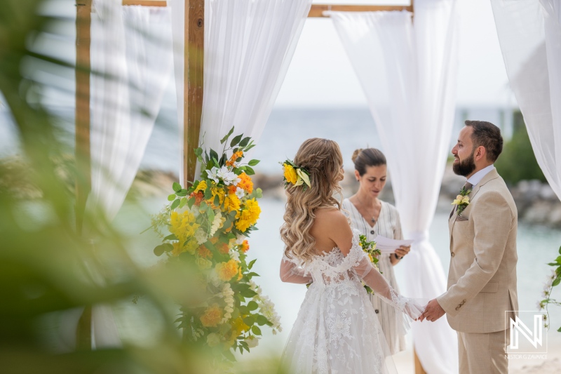 A Beautiful Coastal Wedding Ceremony Taking Place With the Couple Exchanging Vows Under a Floral Arch During a Sunny Day by the Ocean