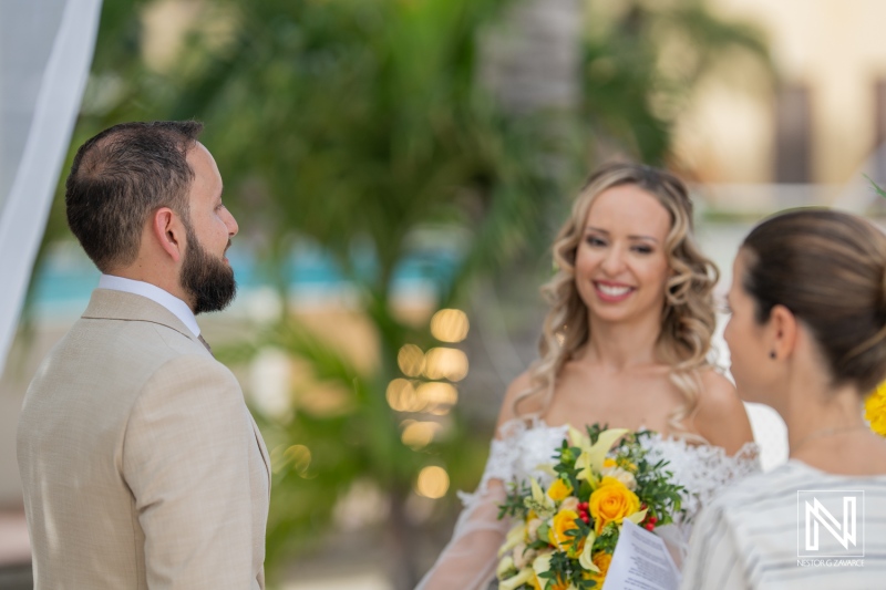 A Couple Exchanges Vows During Their Wedding Ceremony at a Tropical Outdoor Venue Surrounded by Lush Greenery and Blooming Flowers in the Afternoon Sunlight