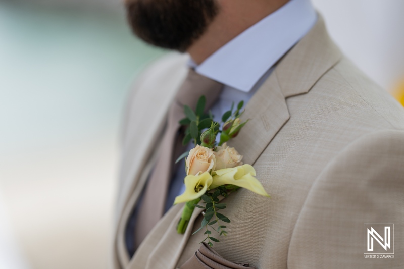 A Well-Dressed Man in a Light Beige Suit With a Floral Boutonniere, Ready for a Formal Event by a Coastal Venue During the Daytime