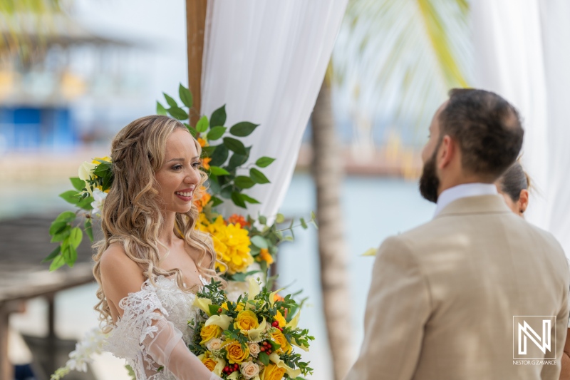 A Joyful Couple Exchanges Vows at a Beach Wedding, Surrounded by Colorful Flowers and Tropical Scenery on a Bright Sunny Day