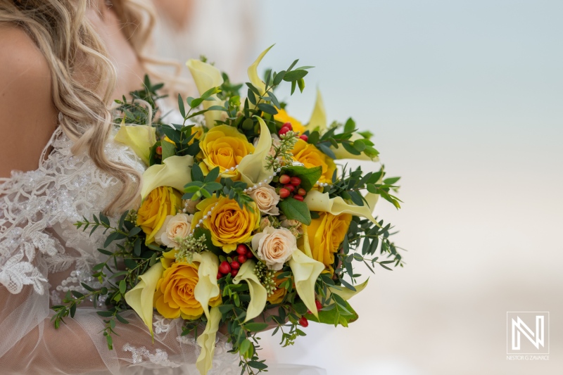 A Close-Up View of a Bride Holding a Vibrant Bouquet of Yellow Roses and Calla Lilies With Greenery at a Beachside Ceremony During Daylight