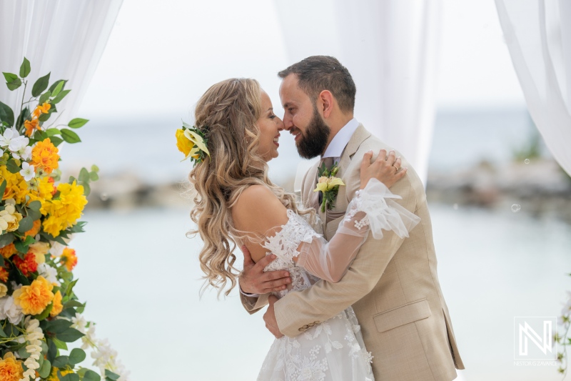 A Joyful Couple Embraces During Their Outdoor Wedding Ceremony by the Waterfront, Surrounded by Floral Decorations in a Sunny, Picturesque Setting