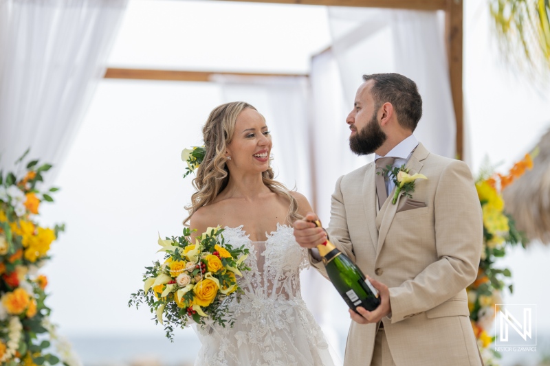 A Joyful Couple Celebrating Their Wedding With Champagne on a Beach During a Sunny Ceremony Surrounded by Flowers