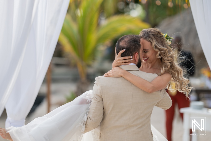 A Joyful Couple Celebrates Their Wedding by Sharing an Intimate Moment on a Sunny Beach Surrounded by Palm Trees and Decorations in a Picturesque Setting