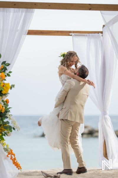 A Couple Celebrates Their Wedding by the Beach, Capturing a Moment of Joy as the Groom Lifts the Bride in a Romantic Embrace During Their Outdoor Ceremony