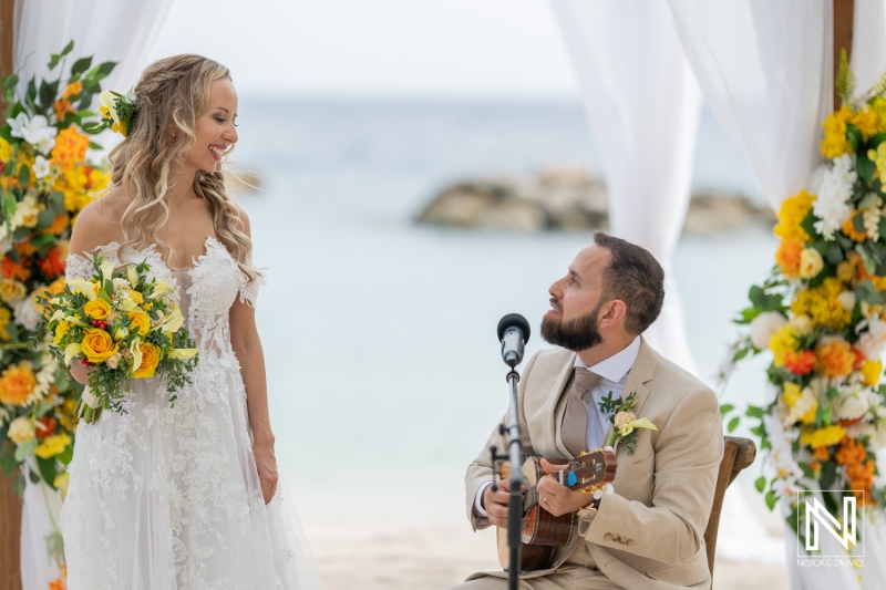 Couple Celebrating Their Wedding Ceremony on a Beach With a Picturesque Backdrop and a Musician Playing for Their Special Moment