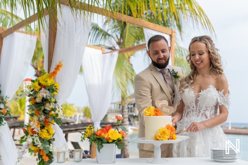 Couple Cuts Wedding Cake at a Beachfront Ceremony Adorned With Tropical Flowers, Celebrating Their Special Day in a Picturesque Setting