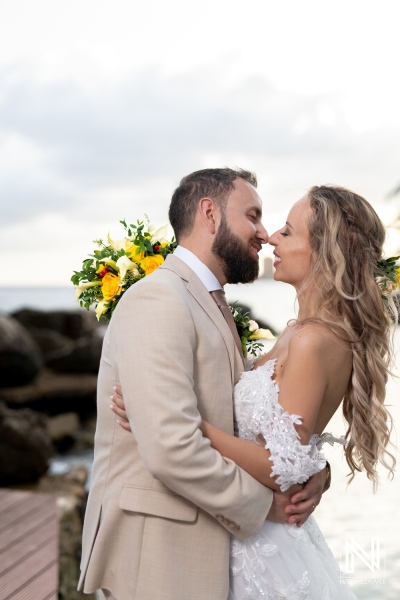 A Joyful Couple Embraces in a Romantic Moment During Their Beachfront Wedding Ceremony at Sunset, Surrounded by Tropical Scenery and Floral Arrangements