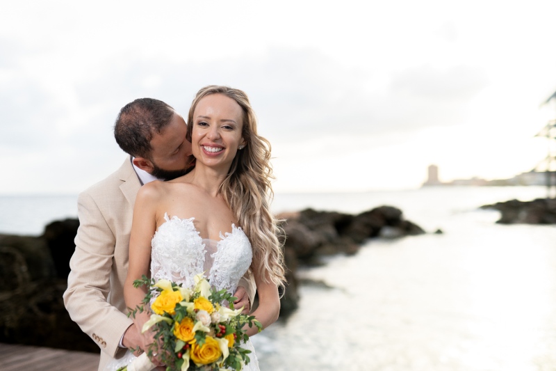 A Joyful Couple Shares a Romantic Moment by the Water During Their Sunset Wedding Ceremony at a Scenic Coastal Location