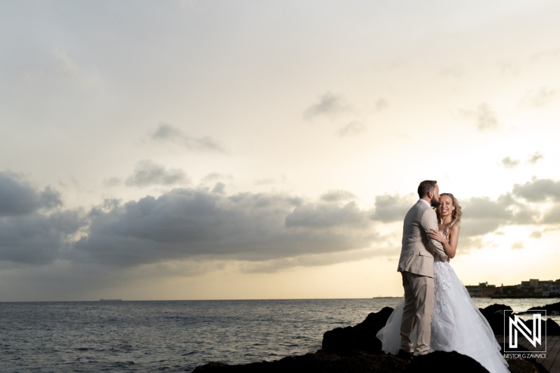 Couple Embracing on Rocky Coastline With Dramatic Skies During Wedding Celebration at Sunset Near the Ocean