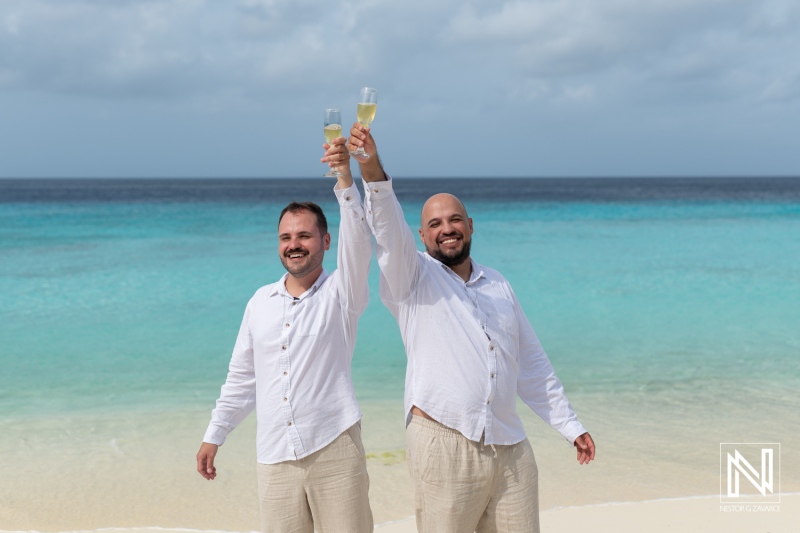 LGBT wedding celebration at sunrise on Cas Abao Beach in Curacao featuring two joyful grooms raising glasses by the shore