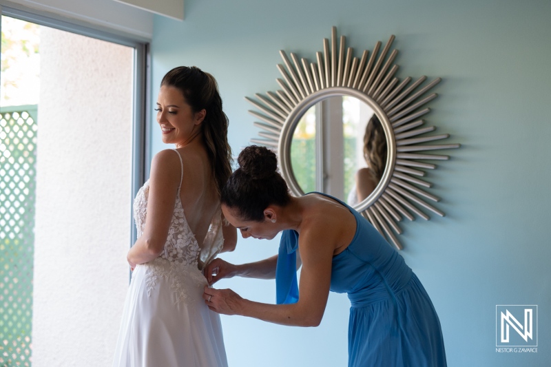 A woman helps another bride with her dress in a bright room with mirror decor, capturing a precious moment before the wedding ceremony