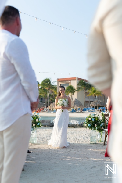 A beautiful bride stands on the beach with palm trees in the background as she prepares to exchange vows during a sunset wedding ceremony