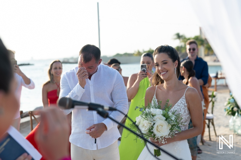 A beautiful beach wedding ceremony takes place as a couple exchanges vows with joy and emotions under a clear sky by the sea during sunset