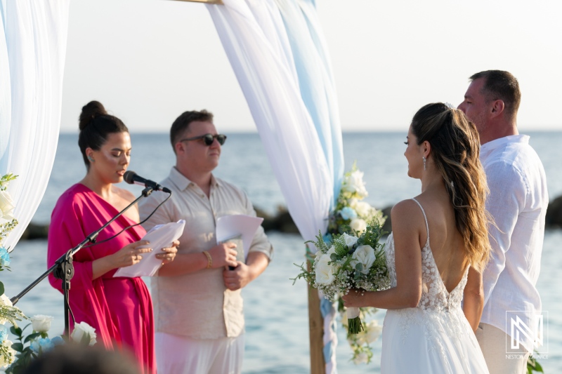 Beach wedding ceremony at sunset with bride, groom, and officiant delivering vows in an intimate coastal setting