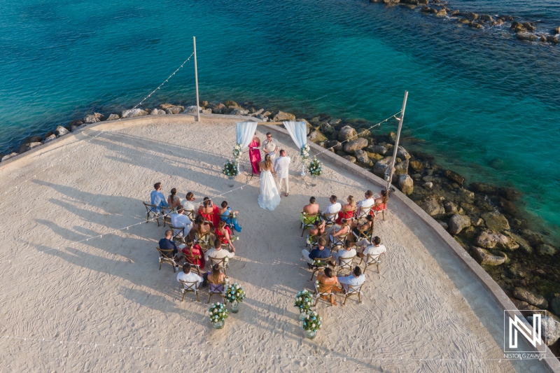 A beautiful beach wedding ceremony with guests seated on a sandy shore at sunset near the calm turquoise waters of a picturesque coastal location