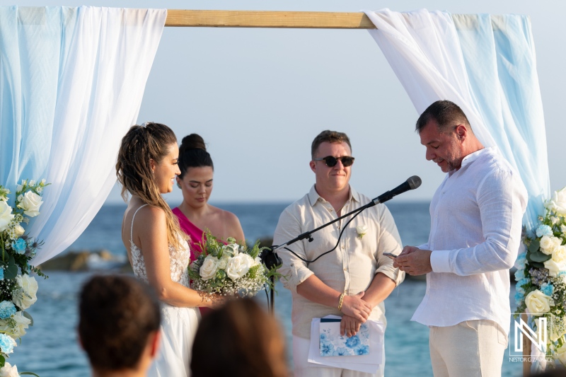 Couple exchanges vows during a romantic beach wedding ceremony in a serene coastal setting with floral decorations and cheerful guests in attendance