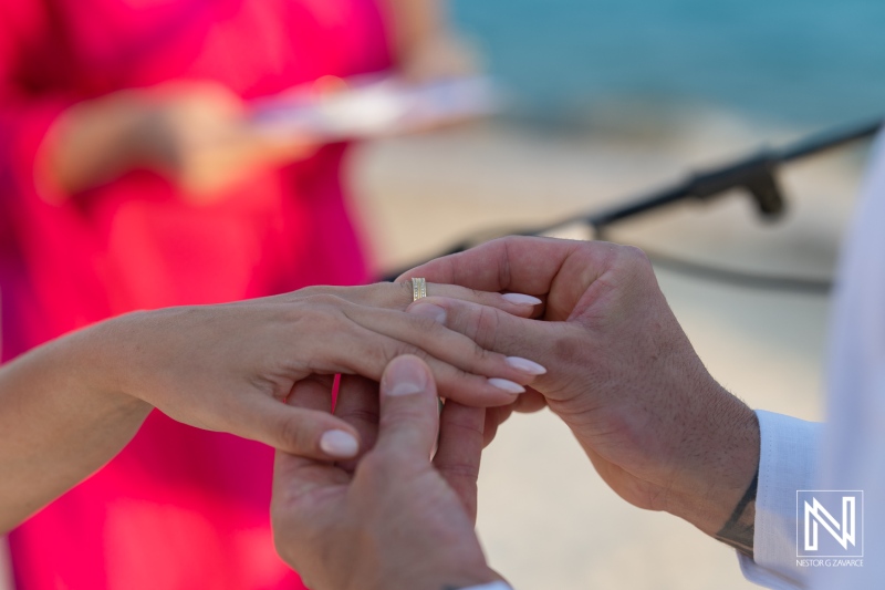 Couple exchanges wedding rings during a beach ceremony at sunset with family and friends witnessing the special moment