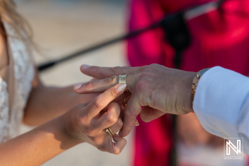 A couple exchanges wedding rings during a sunset ceremony at a beach, showcasing love and commitment in a beautiful outdoor setting with soft waves in the background