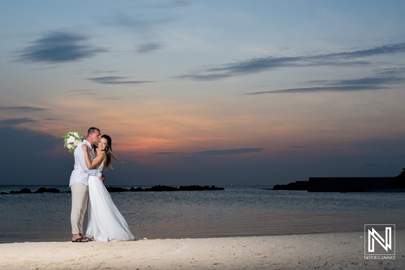 A romantic sunset beach wedding ceremony with a couple embracing as the sun sets over the ocean in a beautiful tropical setting