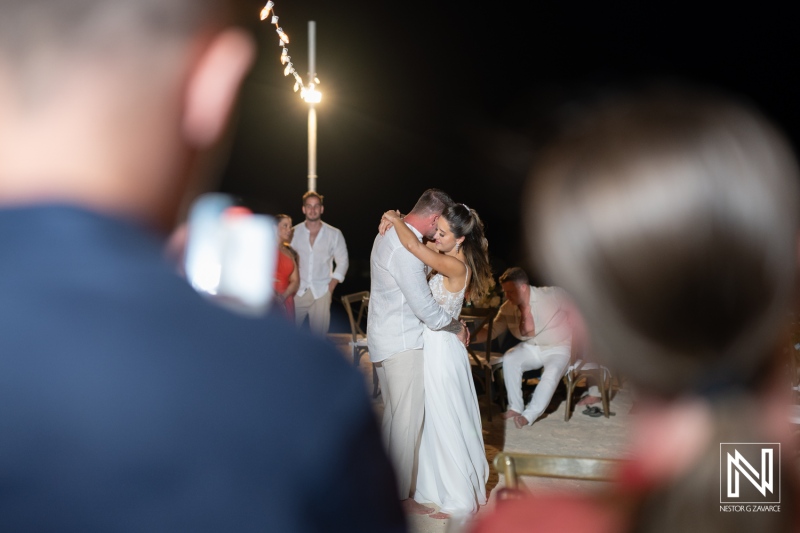 A couple shares a tender embrace during their wedding reception under the warm evening lights at an outdoor venue, celebrating their union with family and friends