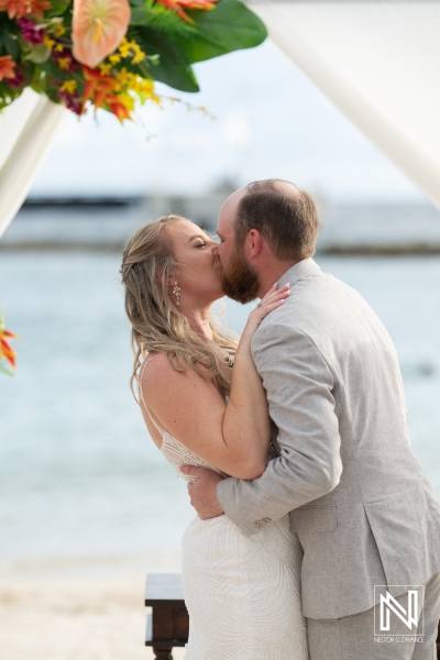 Wedding celebration on the beach at Curacao featuring a loving couple under a floral arch
