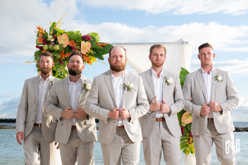 Groom and groomsmen prepare for wedding ceremony at Mangrove Beach in Curacao with beautiful floral backdrop
