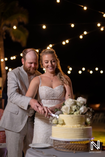 Couple cutting wedding cake under string lights at The Rif at Mangrove Beach, Curacao during a romantic evening celebration