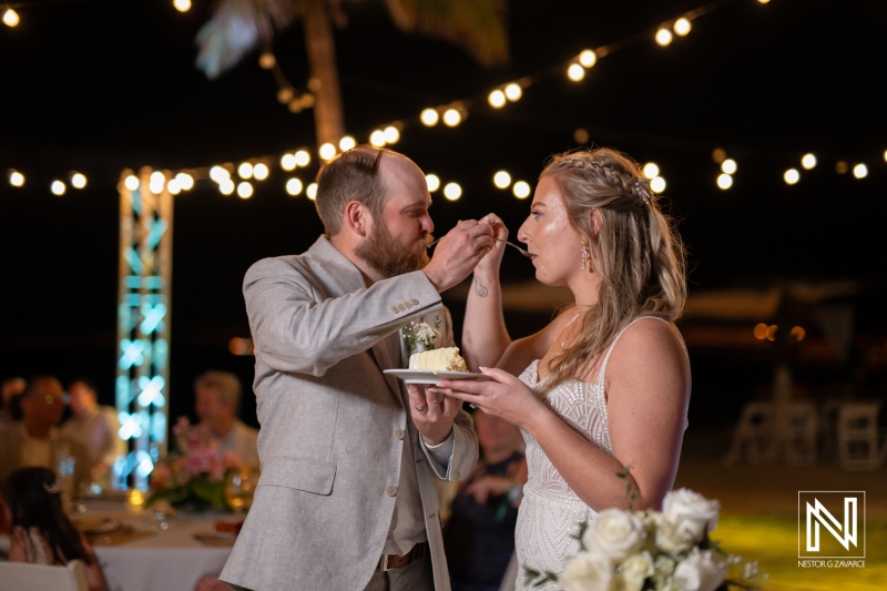Joyful wedding celebration at Mangrove Beach in Curacao featuring a couple sharing their cake during a beautiful evening gathering with family and friends