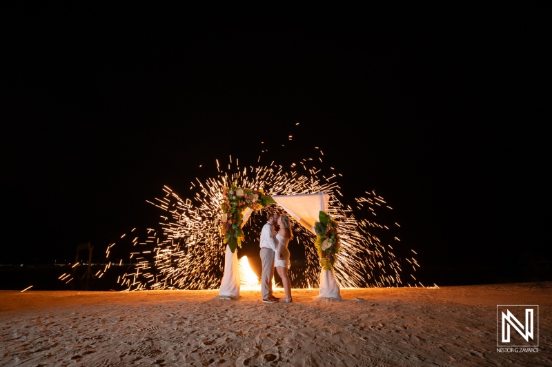 Romantic wedding ceremony at sunset on Curacao beach with beautiful floral arch and stunning sparkler display