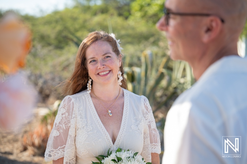 Couple exchanges vows during wedding ceremony in Westpunt Curacao under bright sun with greenery in background