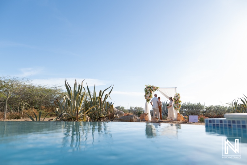 Wedding ceremony takes place in Westpunt Curacao with couple and guests near a pool area under a decorated arch