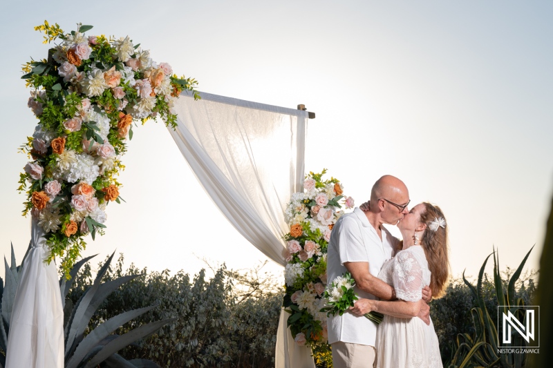 Couple shares a kiss during their wedding ceremony in Westpunt Curacao at sunset with floral decorations surrounding them