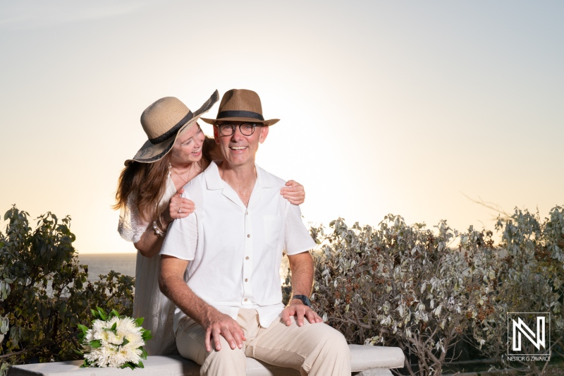 Couple poses for wedding portrait at sunset in Westpunt Curacao wearing hats and holding flowers