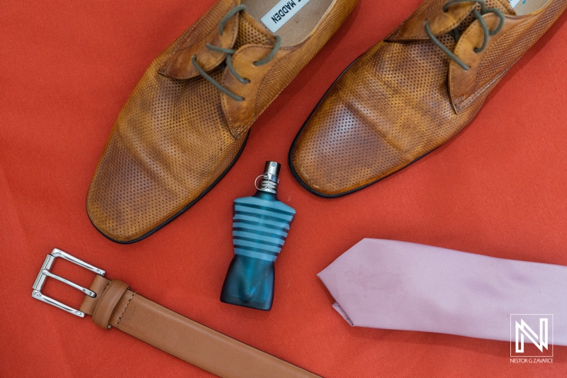 Special wedding details at Dreams Curaçao Resort with shoes, belt, tie, and cologne on orange background