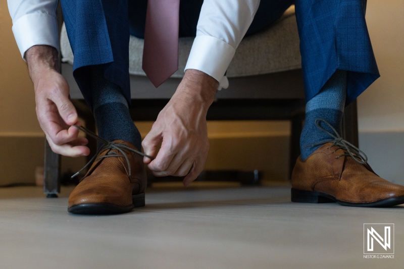Groom prepares for wedding ceremony at Dreams Curaçao Resort with focus on shoe tying