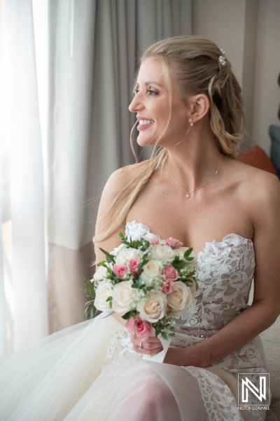 Bride prepares for wedding at Dreams Curacao Resort with bouquet in hand by window in the morning light