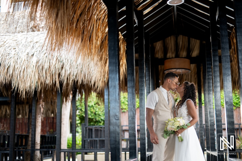 Couple shares a romantic kiss under a thatched roof at Sunscape Curacao Resort during their wedding celebration