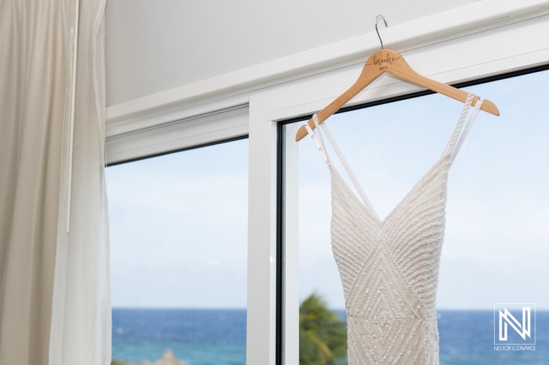 Elegant wedding dress adorns the window overlooking the serene waters of Avila Beach Hotel during a beautiful sunset in Curacao