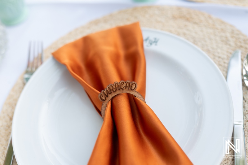 Beautifully arranged table setting with an orange napkin and personalized decoration at a sunset wedding in Curacao