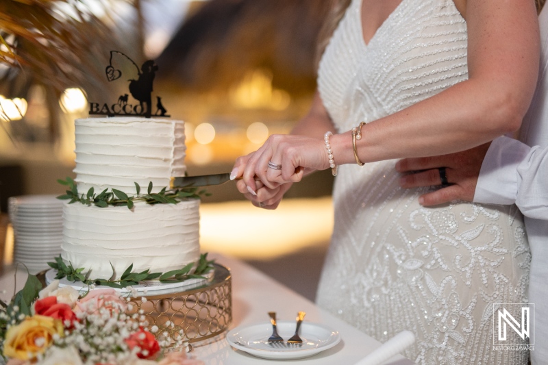 Couple shares a joyful moment while cutting the wedding cake at Avila Beach Hotel during a stunning sunset in Curacao
