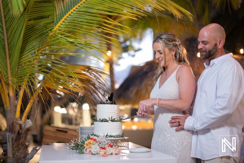 Couple joyfully cutting their wedding cake at the Avila Beach Hotel during a beautiful sunset in Curacao