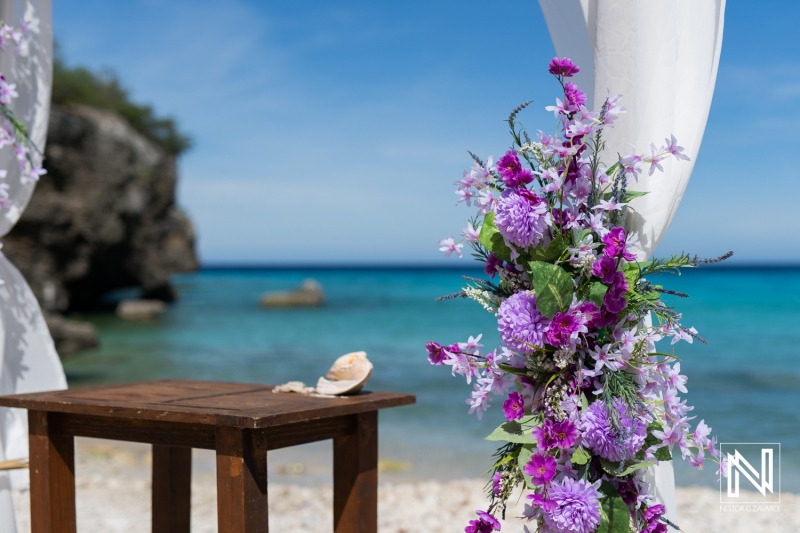 A Serene Beach Wedding Setup Adorned With Vibrant Flowers Under a Clear Blue Sky Near a Rocky Shoreline