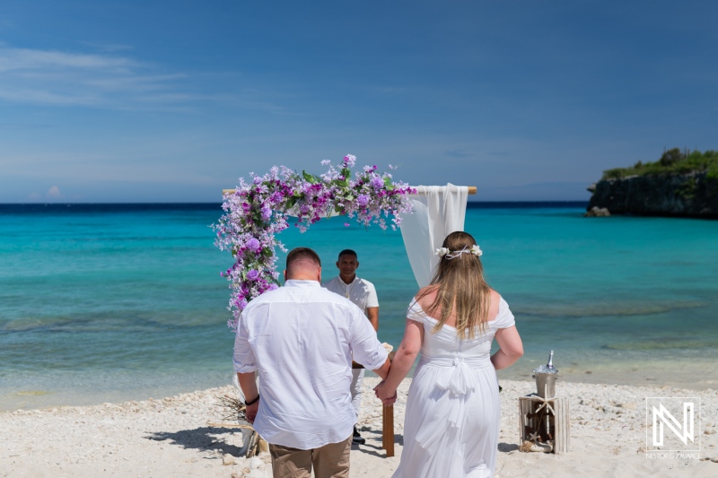 Couple Exchanging Vows During a Beach Wedding Ceremony in a Tropical Location With a Floral Arch and Clear Blue Water in the Background