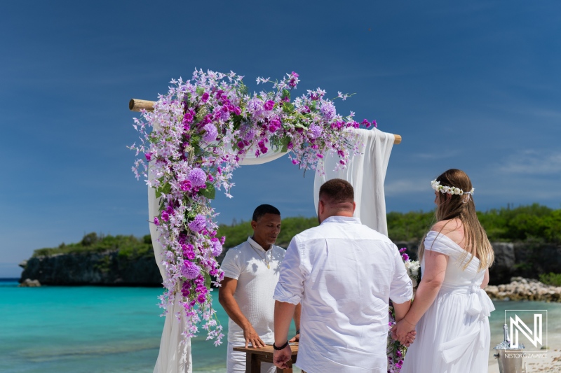 A Couple Exchanging Vows at a Picturesque Beach Wedding Adorned With Floral Decoration During a Sunny Afternoon