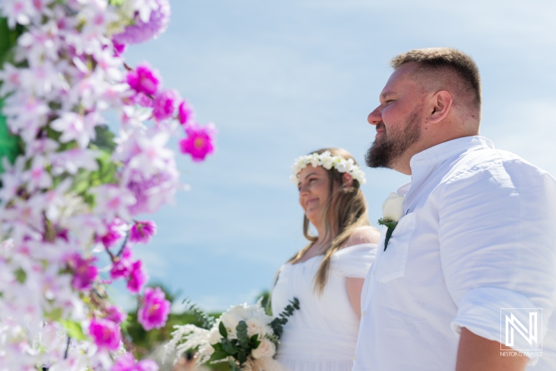 A Couple Stands Together in an Outdoor Wedding Ceremony Surrounded by Flowers and a Clear Blue Sky, Celebrating Their Love in a Beautiful Setting